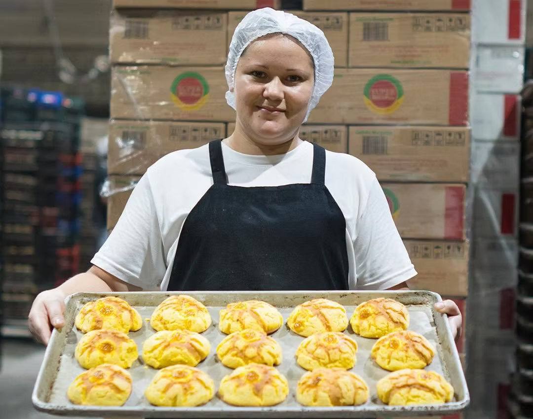 Integrante del equipo de Panificadora Superman con una bandeja de pan frente a cajas de producto